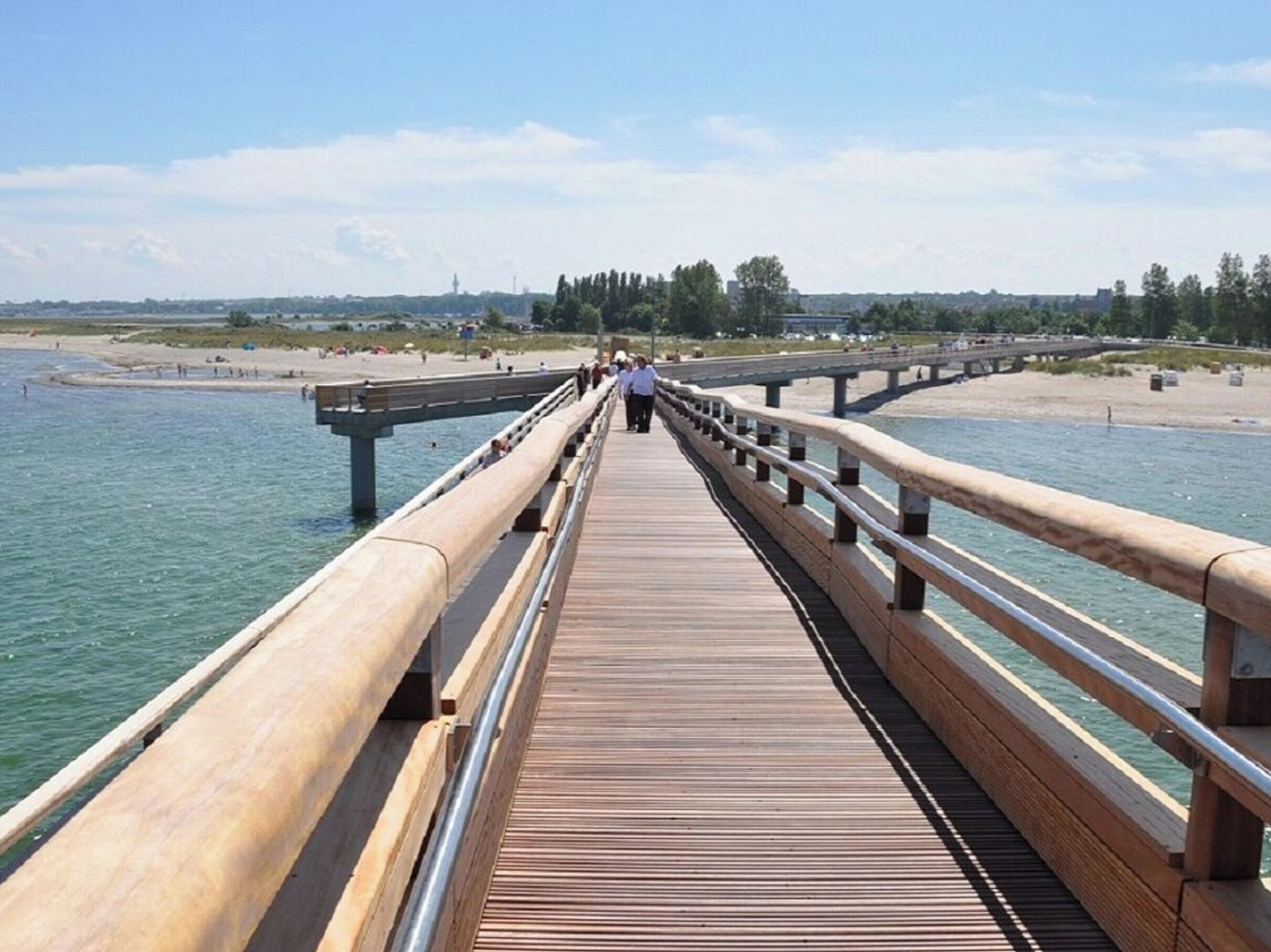 A wooden boardwalk leading to a beach with a clear view of the water and distant buildings.