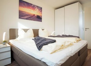 A bedroom with a bed, a nightstand, a wardrobe, and a painting on the wall. - Holiday Apartment With 2 Bedrooms (Heiligenhafen)