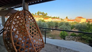 A hanging chair on a balcony overlooking a residential area with houses and greenery. - Stone house with an olive grove, a movie theater, and a sim racing setup—sleeps 8 near Serra da Estrela (Distrito da Guarda)