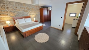 A bedroom with a stone wall, a bed with a wooden headboard, a bedside table with a lamp, and a round rug. - Stone house with an olive grove, a movie theater, and a sim racing setup—sleeps 8 near Serra da Estrela (Distrito da Guarda)