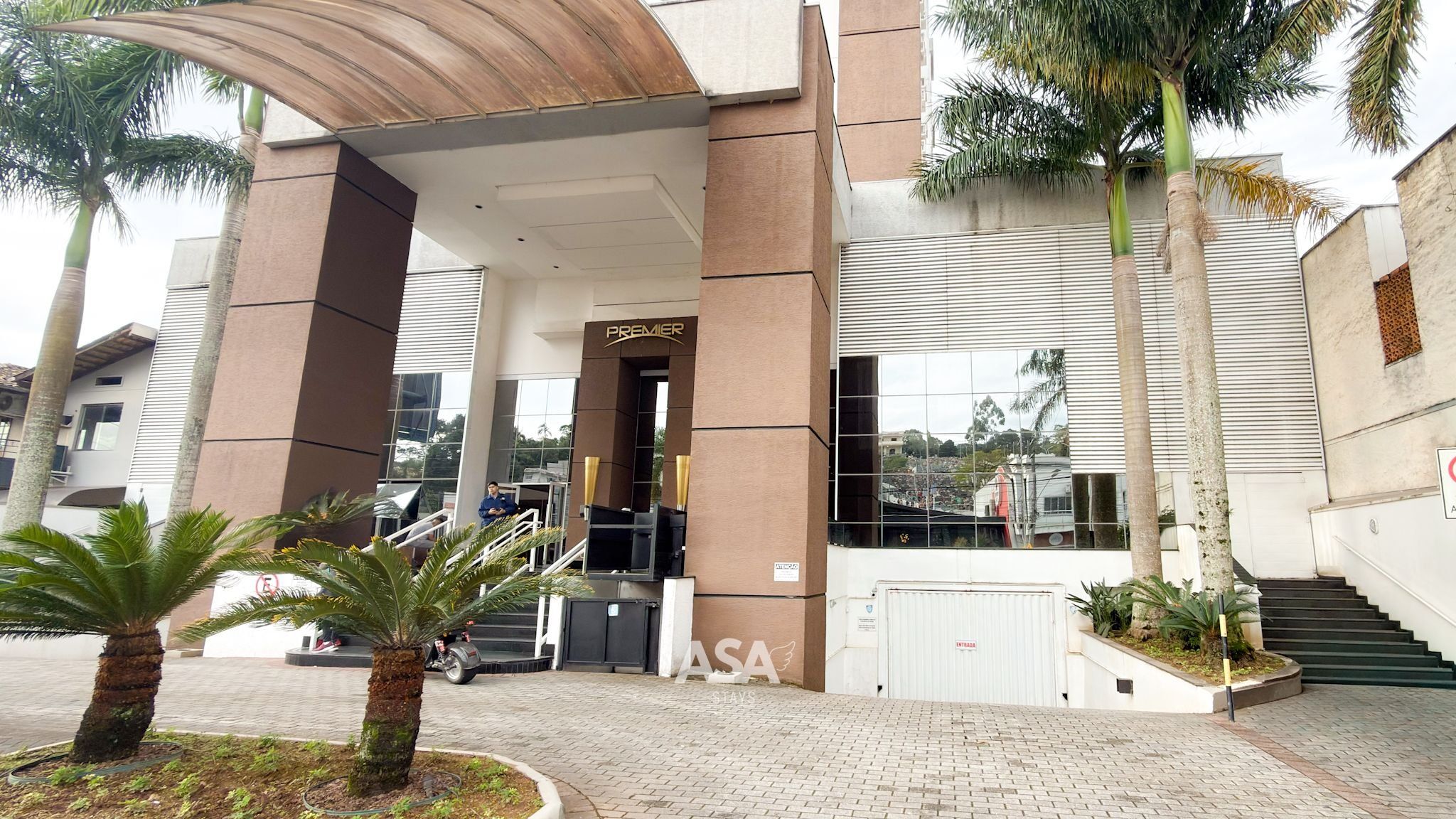 A hotel entrance with a modern design, featuring a prominent 'PREMIER' sign, a covered walkway, and a staircase leading to the entrance.