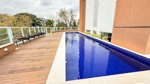A swimming pool with a wooden deck and metal chairs, surrounded by a glass railing. - ASA Premier 610 Loft Blumenau Oktoberfest (Blumenau)