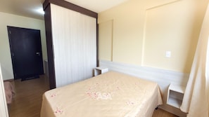 Una habitación de hotel con una cama, una puerta, una mesita de noche y una cortina.