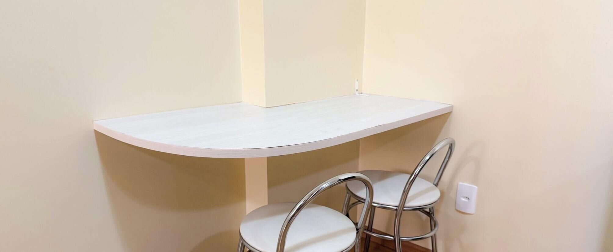 Una esquina de una habitación con una mesa blanca y dos sillas de metal.