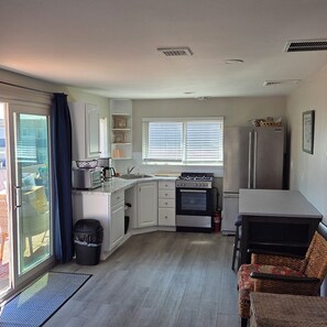 A compact kitchen with a gas stove, oven, and refrigerator. There is a dining table with chairs, a window with blinds, and a door leading to an outdoor area. - 1-bedroom apartment  in Point Pleasant Beach ,walking distance to beach n boards (Point Pleasant Beach)