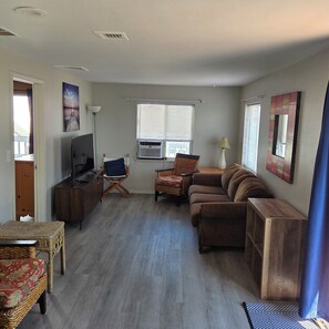 A living room with a television, a sofa, a chair, a table, and a window with blinds. - 1-bedroom apartment  in Point Pleasant Beach ,walking distance to beach n boards (Point Pleasant Beach)