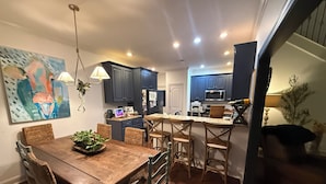 A modern kitchen with dark cabinets, a central island, and a dining area with a wooden table and wicker chairs. - Private 4BR Oxford Home Minutes from Ole Miss & Square (Oxford)
