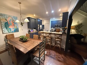 Cocina moderna con armarios oscuros, una isla central y una zona de comedor con mesa de madera y sillas de mimbre.