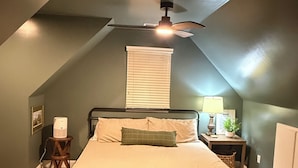 A bedroom with a sloped ceiling, a bed with a headboard, a bedside table with a lamp, and a window with blinds. - Private 4BR Oxford Home Minutes from Ole Miss & Square (Oxford)
