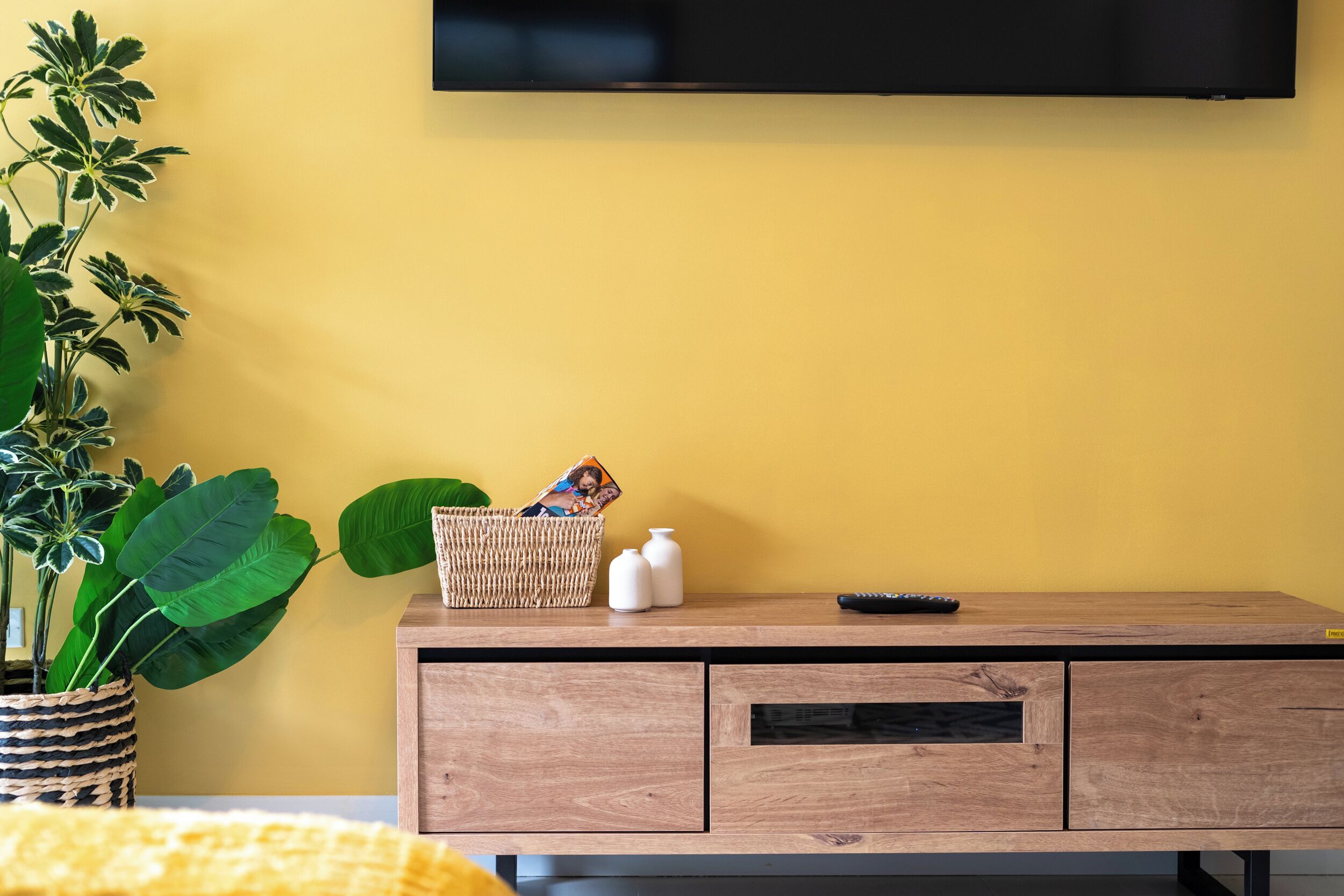 Una habitación con un armario de madera, un televisor montado en la pared y una planta en maceta.