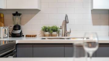 A kitchen with a white countertop, a blender, a toaster, a sink, and a wine glass.