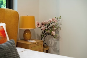 A neatly made bed with a pillow, a bedside lamp, a remote control, and a decorative branch with flowers.