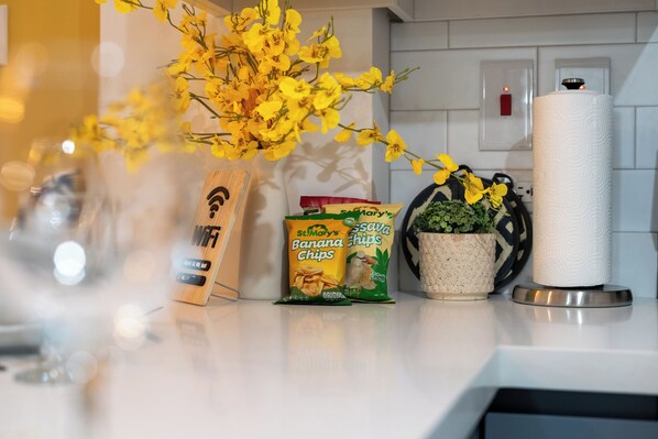 A kitchen counter with a wooden phone, a bag of chips, a potted plant, and a roll of paper towels.