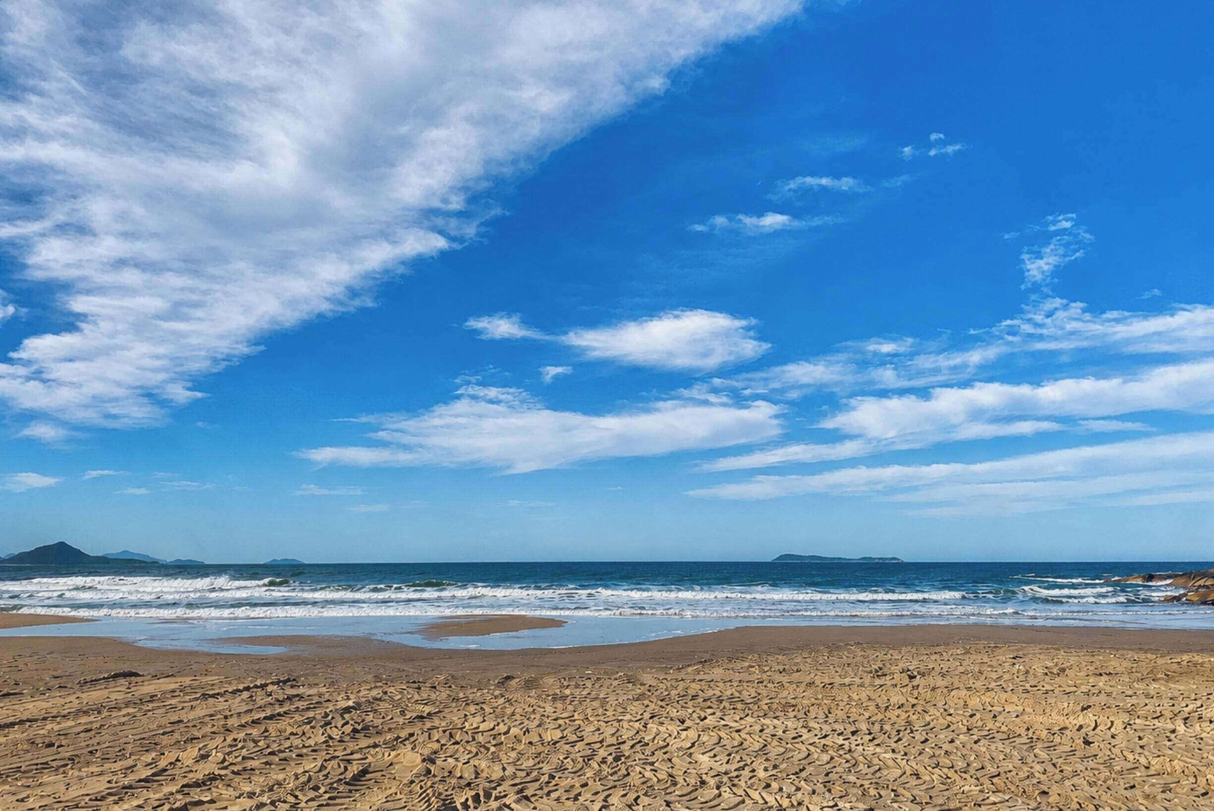 Una playa con olas, cielo despejado y montañas a lo lejos.