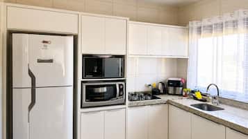 Cozinha moderna com armários brancos, micro-ondas embutido, fogão e geladeira.