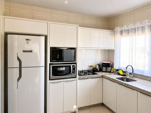 Cozinha moderna com armários brancos, micro-ondas embutido, fogão e geladeira.