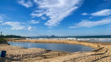 Uma praia com um pequeno lago, terreno arenoso e montanhas ao longe.
