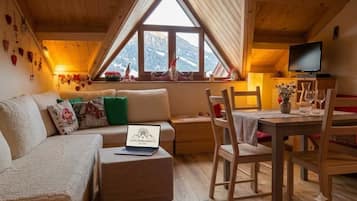 Una stanza accogliente con soffitto in legno, un divano con cuscini, un tavolino con sedie, un portatile e una TV.