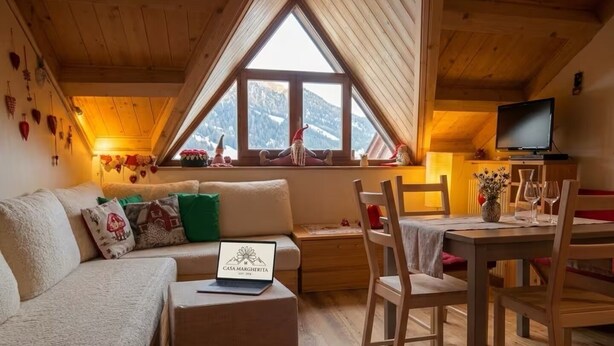 Une pièce chaleureuse avec un plafond en bois, un canapé avec des coussins, une petite table avec des chaises, un ordinateur portable et un téléviseur.
