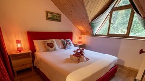 Une chambre avec un plafond en bois, un lit doté d’une tête de lit rouge, deux lampes de chevet et une fenêtre donnant sur des arbres.