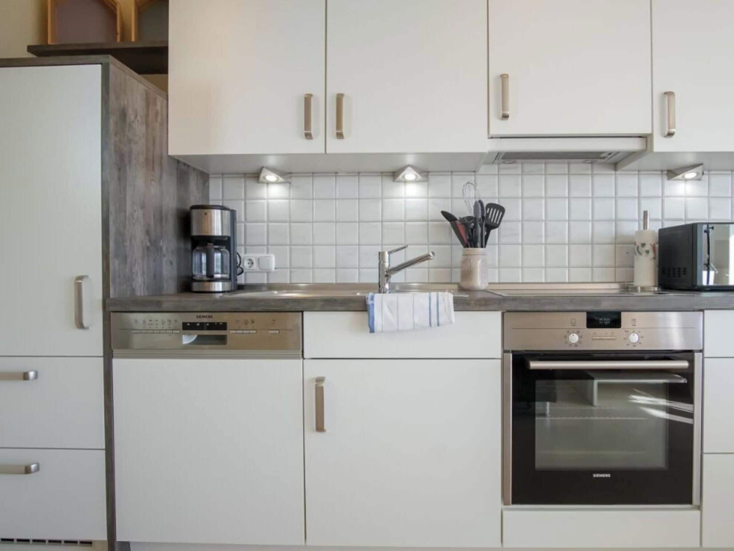Eine moderne Küche mit weißen Schränken, einer Kaffeemaschine, einer Mikrowelle und einem Backofen.