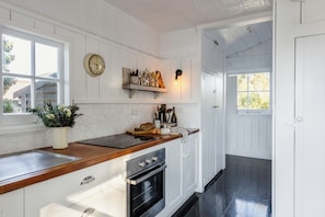 Una cocina con armarios blancos, encimera de madera, horno empotrado y un reloj en la pared.