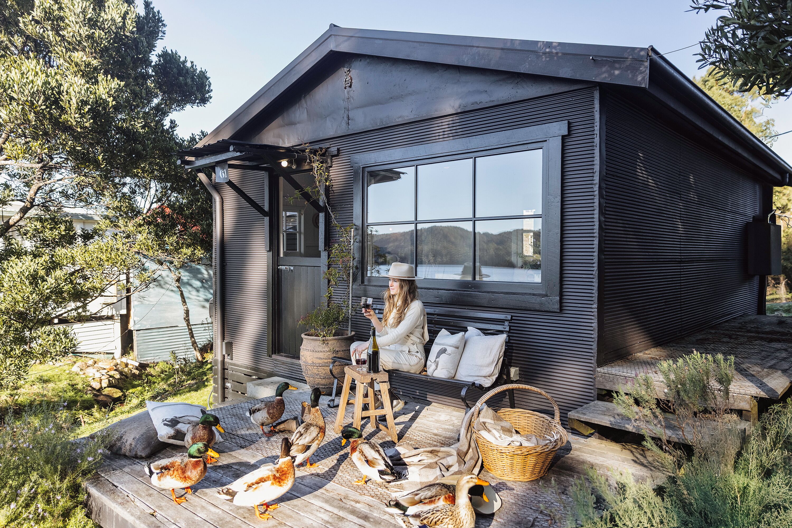 A cabin with a large window, a wooden deck, and ducks on the ground.