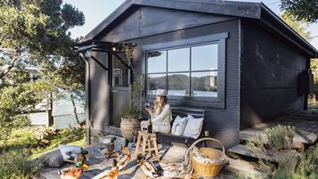 A cabin with a large window, a wooden deck, and ducks on the ground.