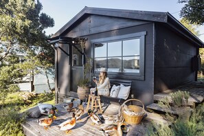 A cabin with a large window, a wooden deck, and ducks on the ground.