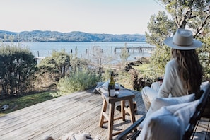 A person sitting on a wooden deck overlooking a lake with a dock and mountains in the distance.