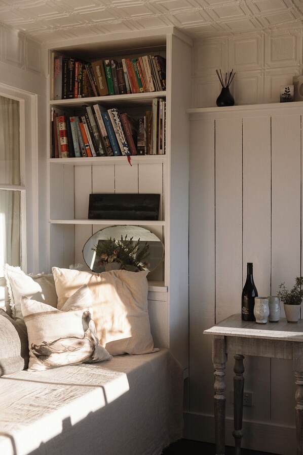 A bedroom with a bed, a bookshelf, a mirror, and a small table with a bottle and a vase.