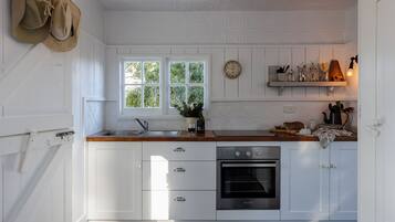 A kitchen with white cabinetry, a stainless steel oven, a window with a view of greenery, and a shelf with kitchen utensils.