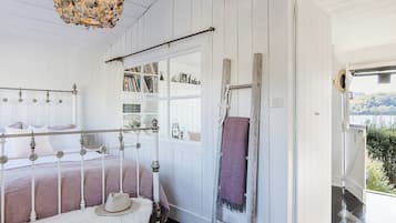 A bedroom with a bed, a wooden ladder, a hanging light fixture, and a view of the outdoors.
