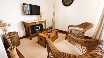 A living room with a flat-screen TV, a wooden coffee table, wicker chairs, a clock on the wall, and a decorative vase.