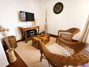 A living room with a flat-screen TV, a wooden coffee table, wicker chairs, a clock on the wall, and a decorative vase. - A cozy and spacious apartment with private access. Pets are welcome. (Río Cuarto)
