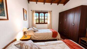 A bedroom with two beds, a window with curtains, a wardrobe, and a lamp.