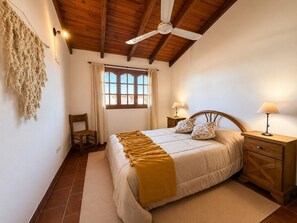 A bedroom with a bed, a ceiling fan, a window with curtains, a chair, and bedside tables with lamps.