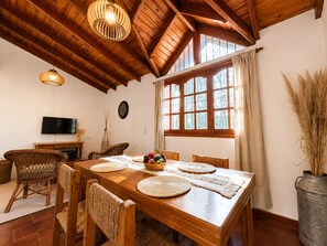 A dining area with a wooden table, woven chairs, and a large window with curtains.