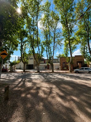 A street lined with trees casting shadows on the ground, with buildings and parked cars in the background. - A cozy and spacious apartment with private access. Pets are welcome. (Río Cuarto)