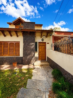 A house with a stone facade, wooden shutters, a stone entrance, and a metal gate.