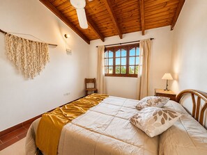 A bedroom with a wooden ceiling, a bed with a yellow blanket, a window with curtains, a chair, and a bedside table with a lamp. - A cozy and spacious apartment with private access. Pets are welcome. (Río Cuarto)