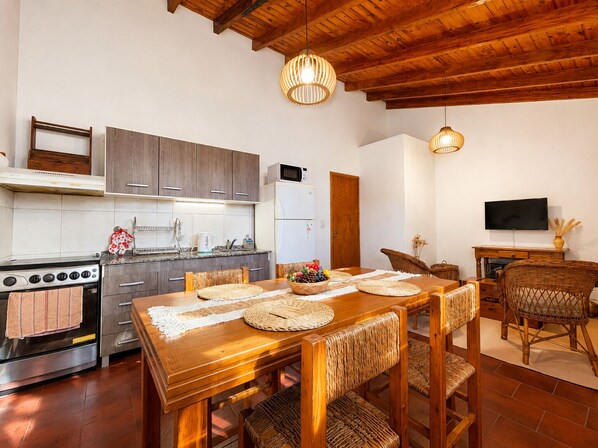 A modern kitchen with a dining area, wooden ceiling, and a flat-screen TV.