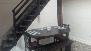 Et spiseområde med et sort bord, ternede servietter og en bænk. En trappe med sorte gelændere ses i baggrunden.