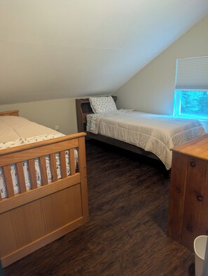 Quarto com duas camas de madeira, janela com persianas e cômoda de madeira.