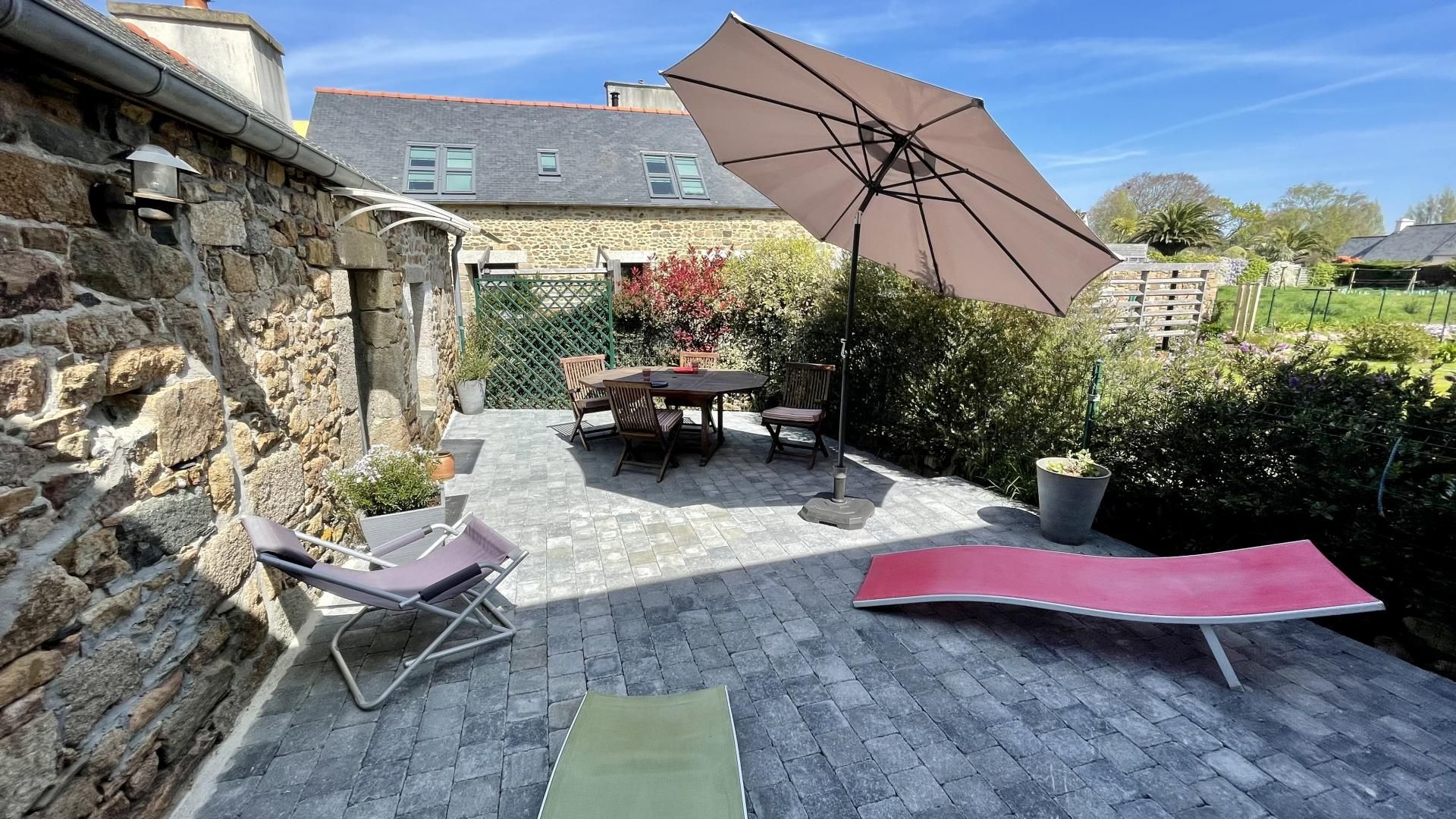 A patio with a table and chairs, a lounge chair, and a large umbrella.