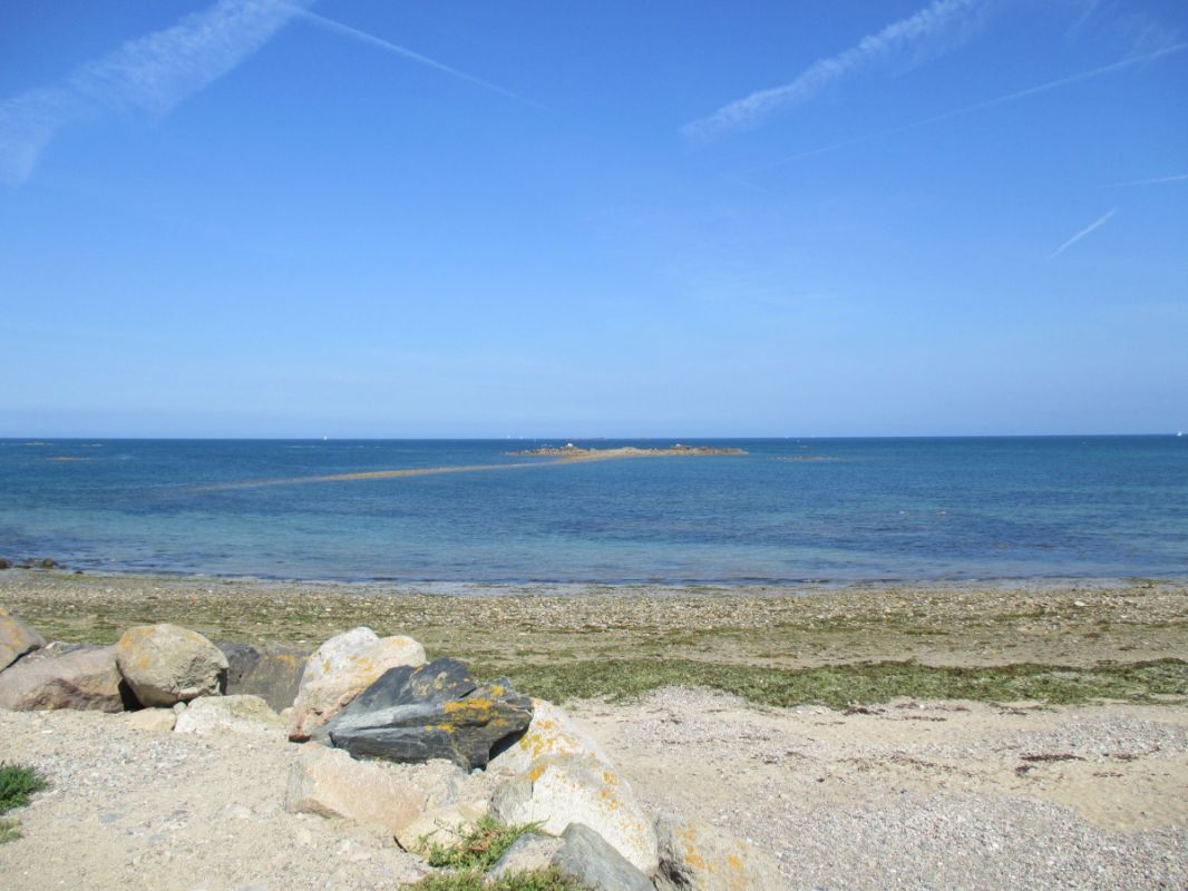 Un paisaje costero con cielo despejado, primer plano rocoso y mar tranquilo.