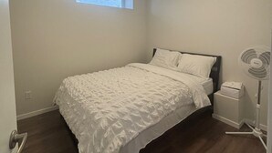Un dormitorio con cama, ventana, lámpara de techo y ventilador de pie.