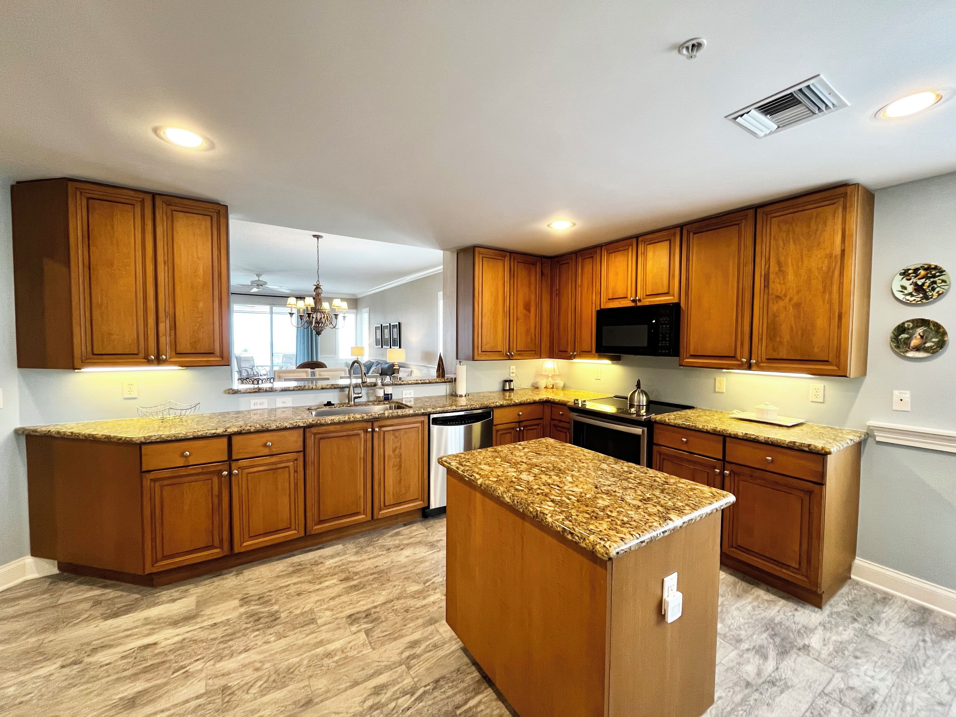 Una cocina moderna con armarios de madera, encimeras de granito, electrodomésticos de acero inoxidable y una isla central.