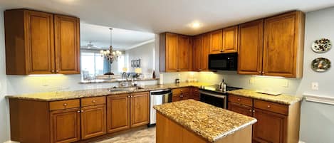 Una cocina moderna con armarios de madera, encimeras de granito, electrodomésticos de acero inoxidable y una isla central.