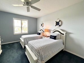 Camera da letto con due letti, una ventola a soffitto, una finestra e decorazioni alle pareti.